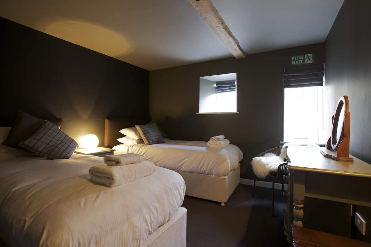 A hotel room with two beds, a desk, a chair, a mirror, and a window with a view.