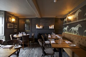 Un restaurant avec des tables et des chaises en bois, une cheminée et des bougies fixées aux murs.