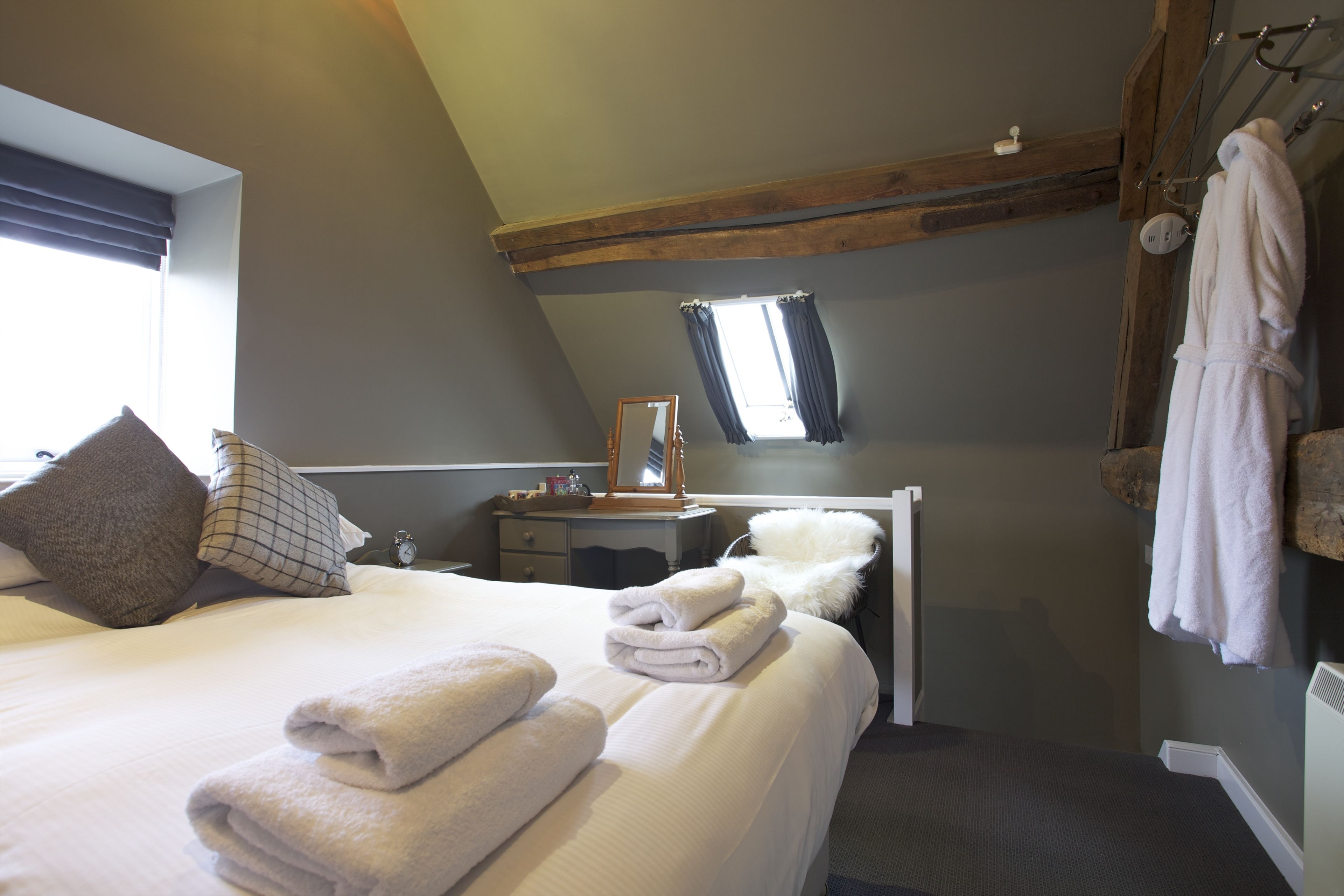 Un dormitorio con una cama, almohadas, una mesita de noche, un espejo, una ventana y un perchero.