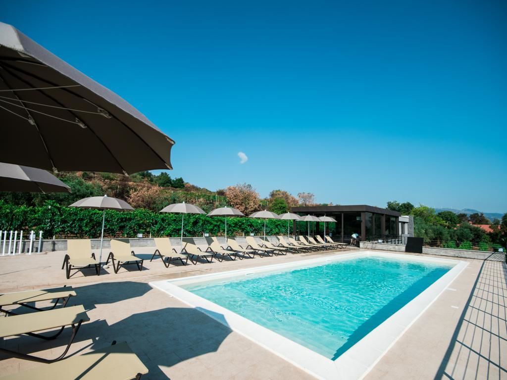 Une piscine entourée de verdure, avec des chaises longues et des parasols, sous un ciel dégagé.