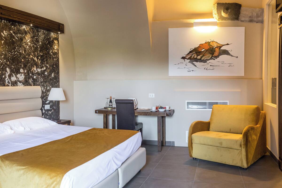 A hotel room with a bed, a desk, a chair, and a painting on the wall.