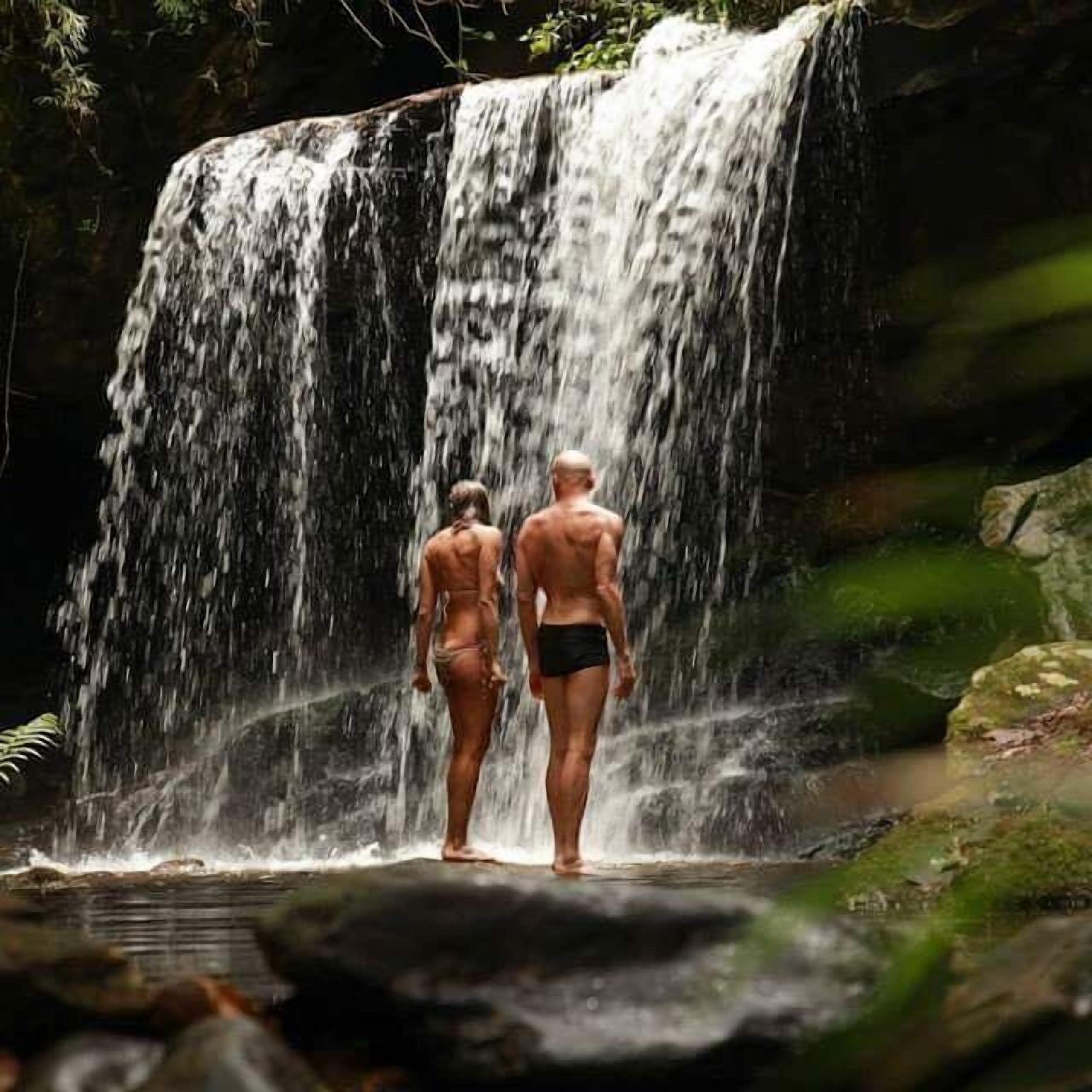 Duas pessoas em frente à base de uma cachoeira.