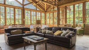 Una habitació àmplia amb grans finestres, sostre de fusta, sofà de pell marró, taula petita i butaca verda.