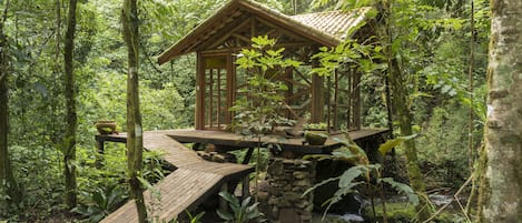A wooden cabin with a sloped roof, built on stilts in a forested area.