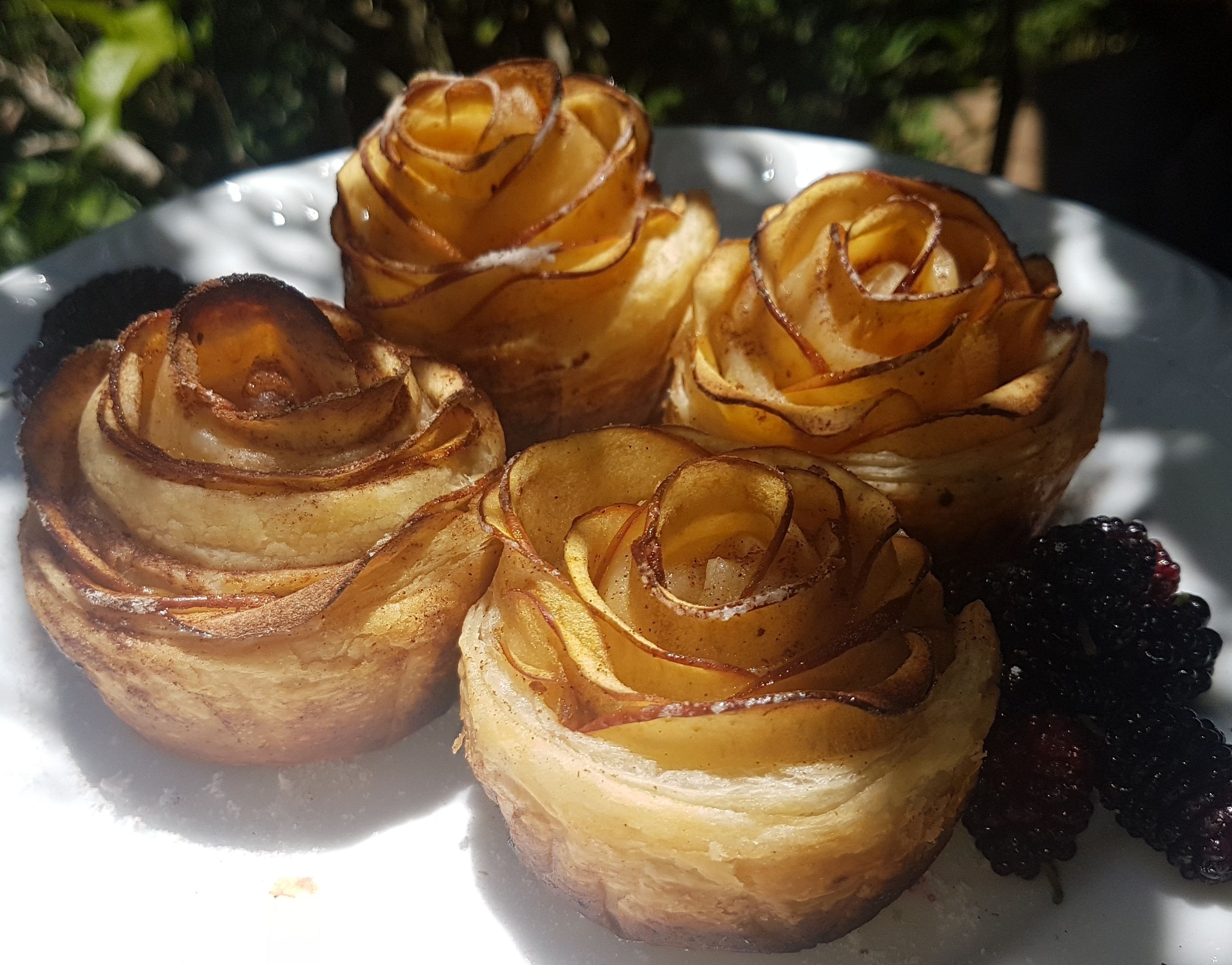 A plate with four rose-shaped pastries and some berries.