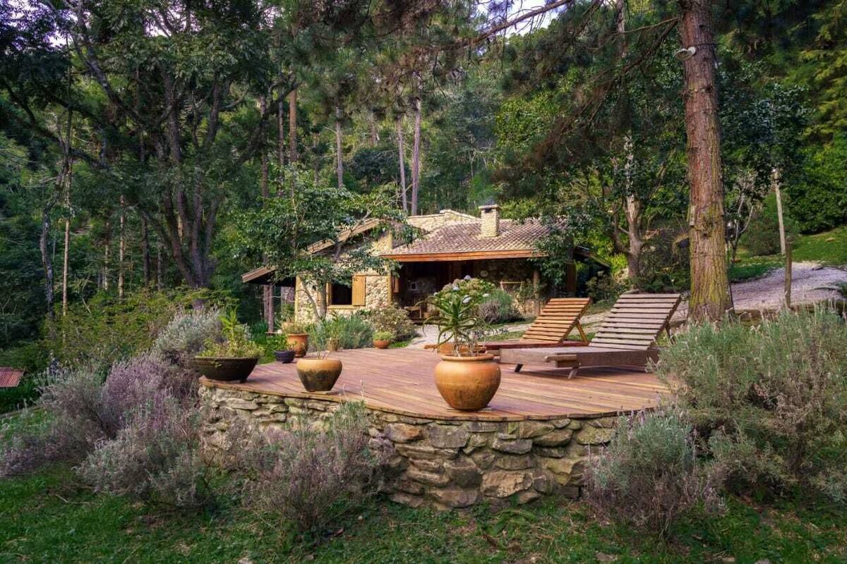 Ein rustikales Blockhaus mit Stein Fundament, einer Holzterrasse und einer Sitzgelegenheit im Freien, umgeben von dichtem Wald.