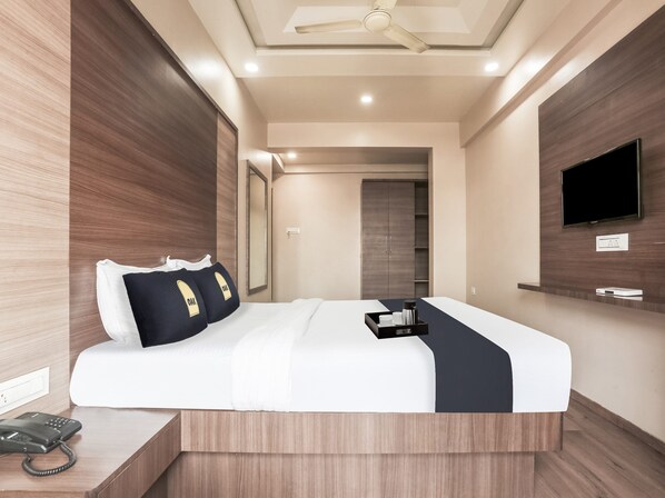 Una habitación de hotel moderna con una cama grande, un televisor de pantalla plana montado en la pared, un teléfono junto a la cama y un ventilador de techo.