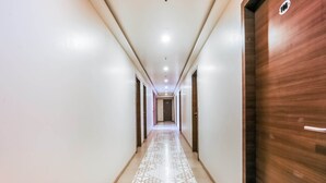 A long, narrow hallway with patterned floor tiles, white walls, and a wooden door on the right. - Hotel Mahadev Residency (Bhiwandi)