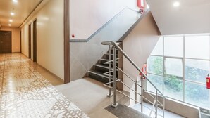 A modern hotel interior with a staircase, patterned carpet, and large windows offering a view of greenery. - Hotel Mahadev Residency (Bhiwandi)