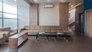 A modern lobby with a beige sofa, glass coffee tables, and a wooden bench. - Hotel Mahadev Residency (Bhiwandi)