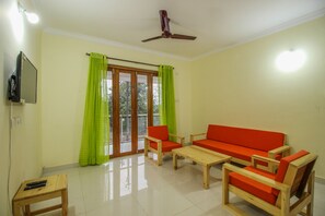A living room with a sofa, chairs, a coffee table, a TV, and a ceiling fan. - OYO 10297 Home Sunset View 2BHK Dona Paula (Panaji)