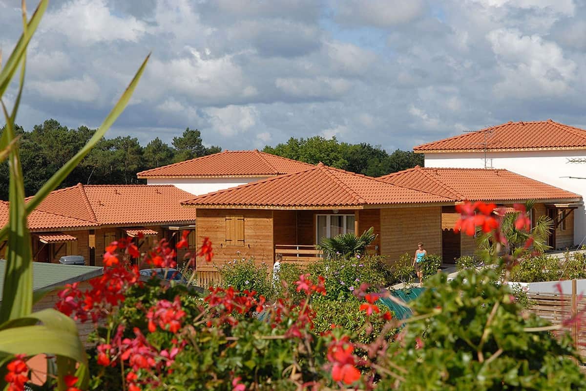 A row of wooden cabins with red-tiled roofs, surrounded by lush greenery and flowering plants.
