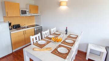 A compact kitchen with wooden cabinets, a microwave, and a dining table set for four with plates, cutlery, and a baguette.