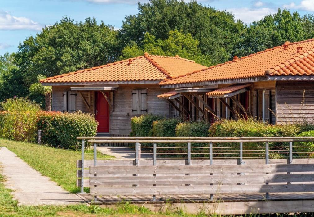 Een houten huis met een rode deur en een pannendak, omgeven door begroeiing.