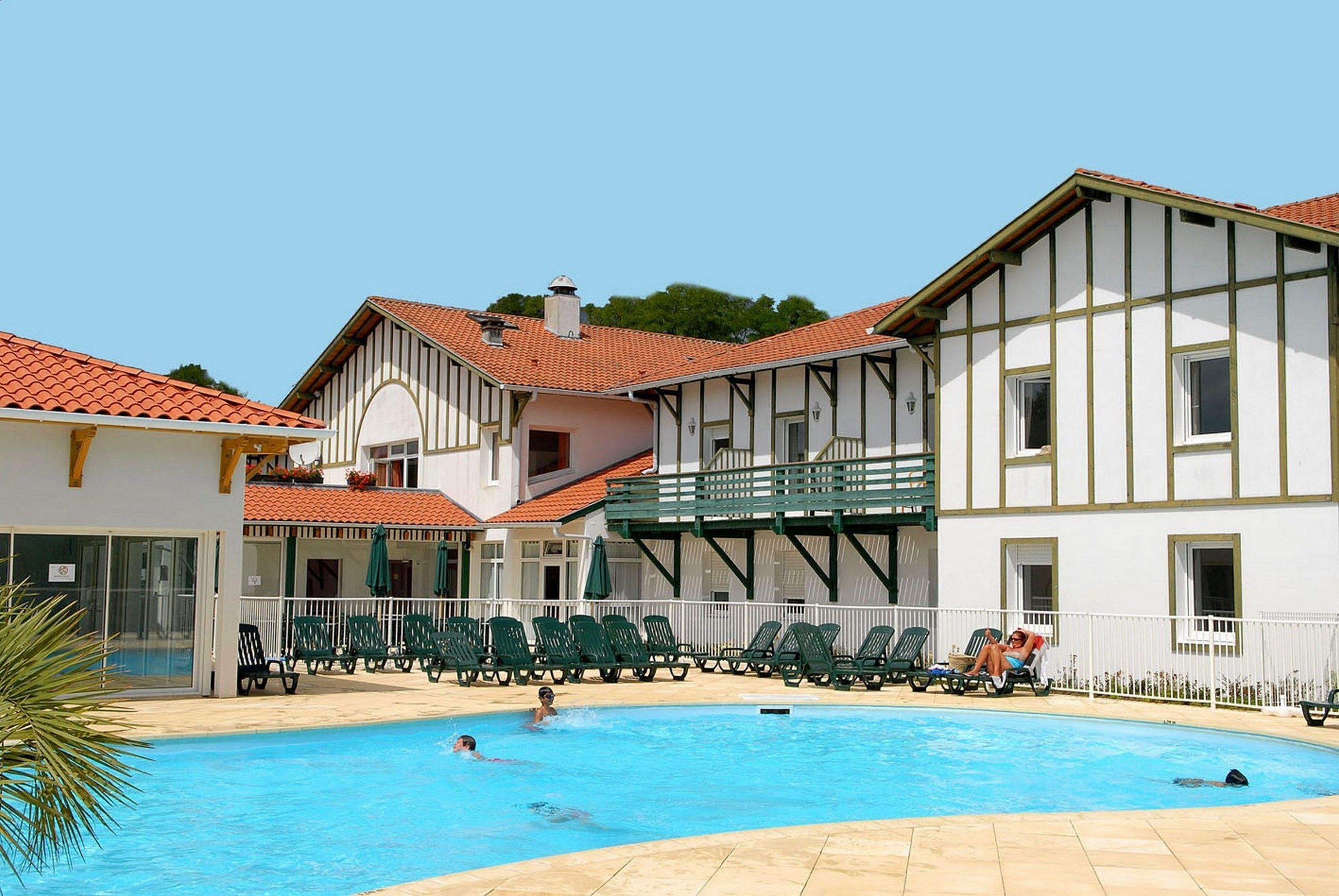 A swimming pool area with lounge chairs and a building with a balcony.