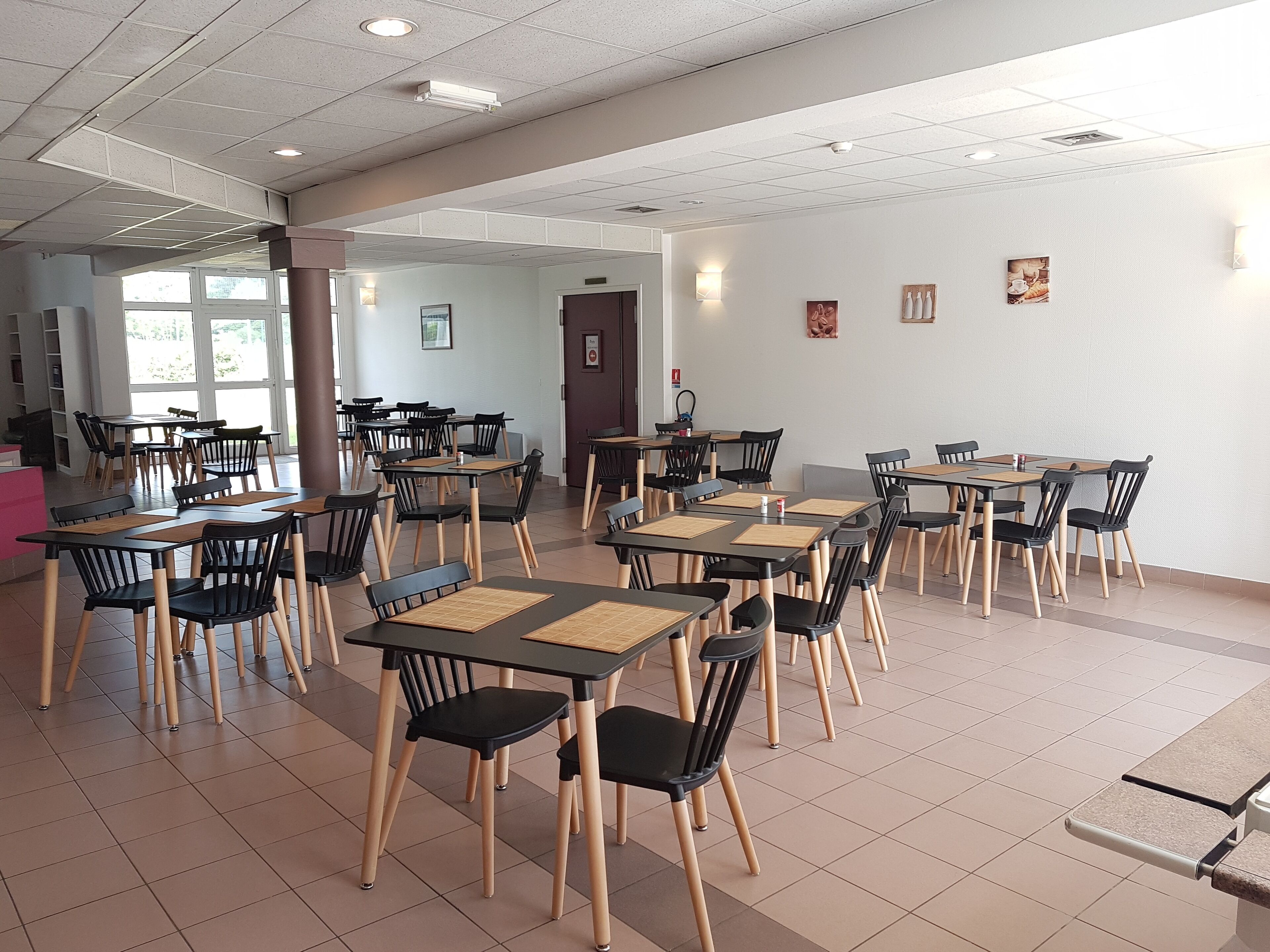 Un grand espace dédié à la salle à manger, avec plusieurs tables et chaises, une porte bien visible et quelques tableaux encadrés accrochés au mur.