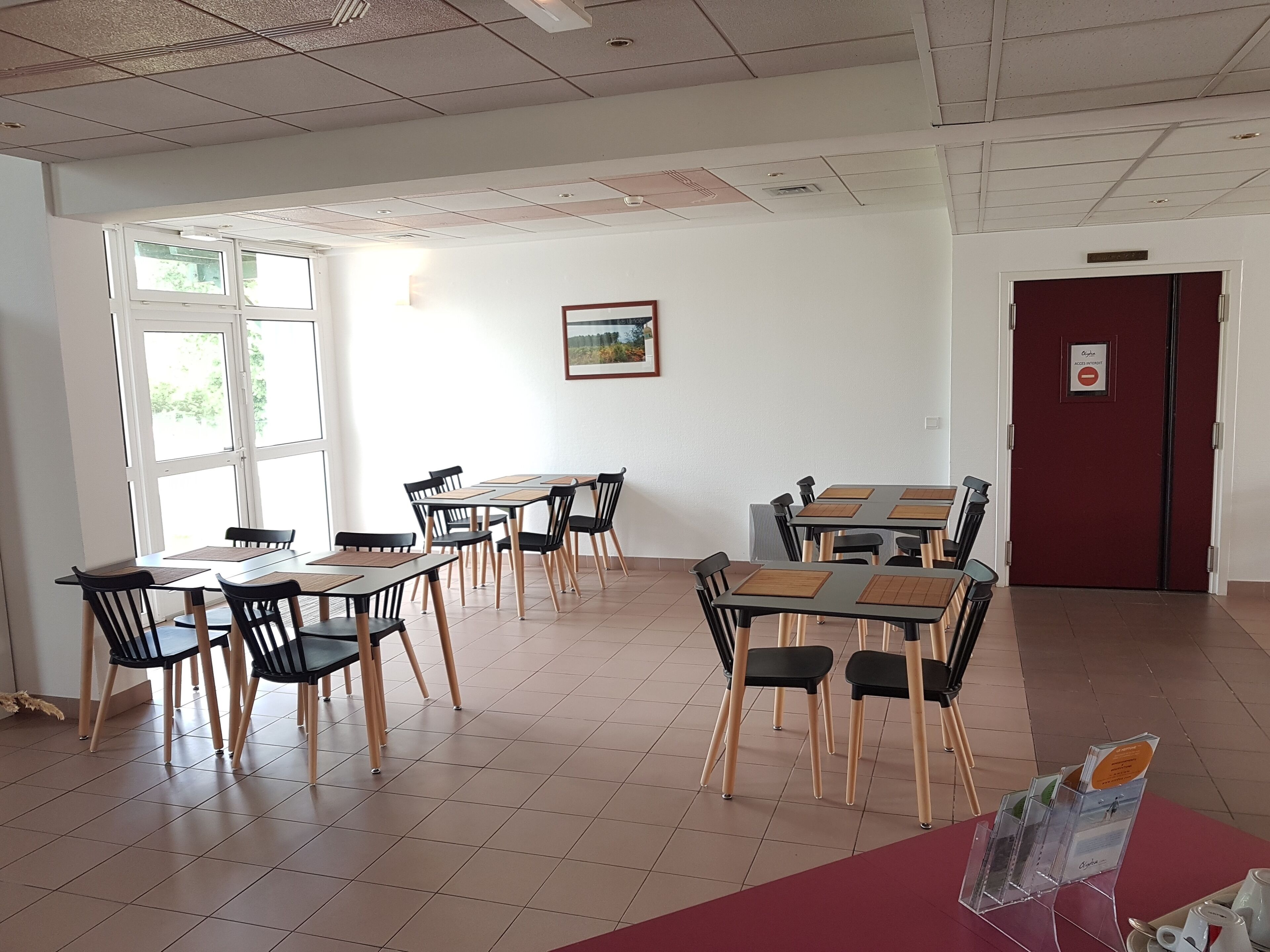 A dining area with multiple tables and chairs, a framed picture on the wall, and a door with a sign.