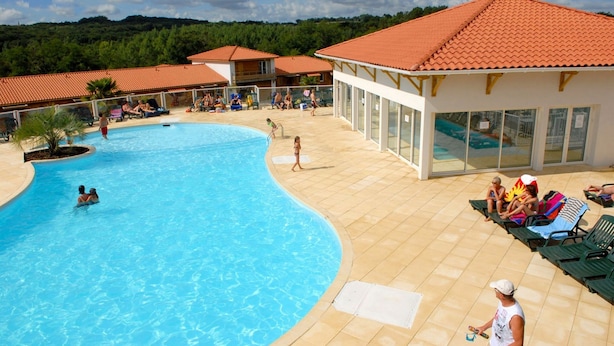 A swimming pool with lounge chairs and a building with a tiled roof. - Olydea Cassen (Cassen)