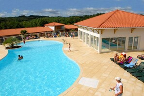 A swimming pool with lounge chairs and a building with a tiled roof. - Olydea Cassen (Cassen)