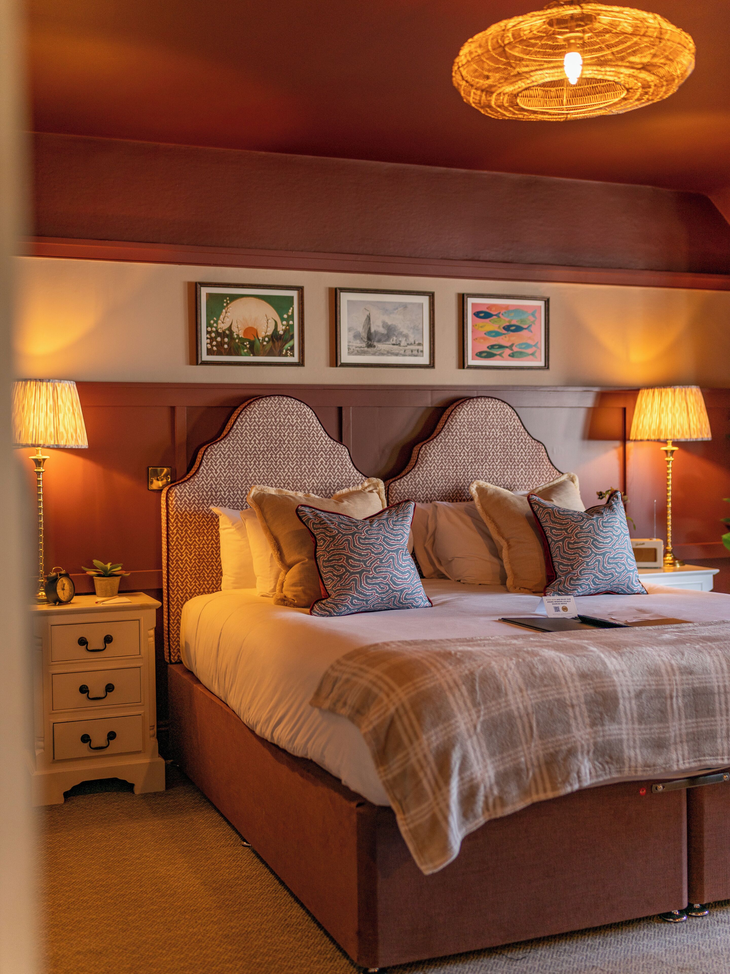 A bedroom with a large bed, two bedside tables, a nightstand, and a wall-mounted lamp.