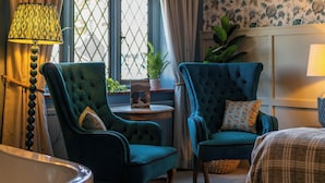A room with two blue armchairs, a round table with a potted plant, a bathtub, and floral wallpaper. - The Mayflower (Lymington)
