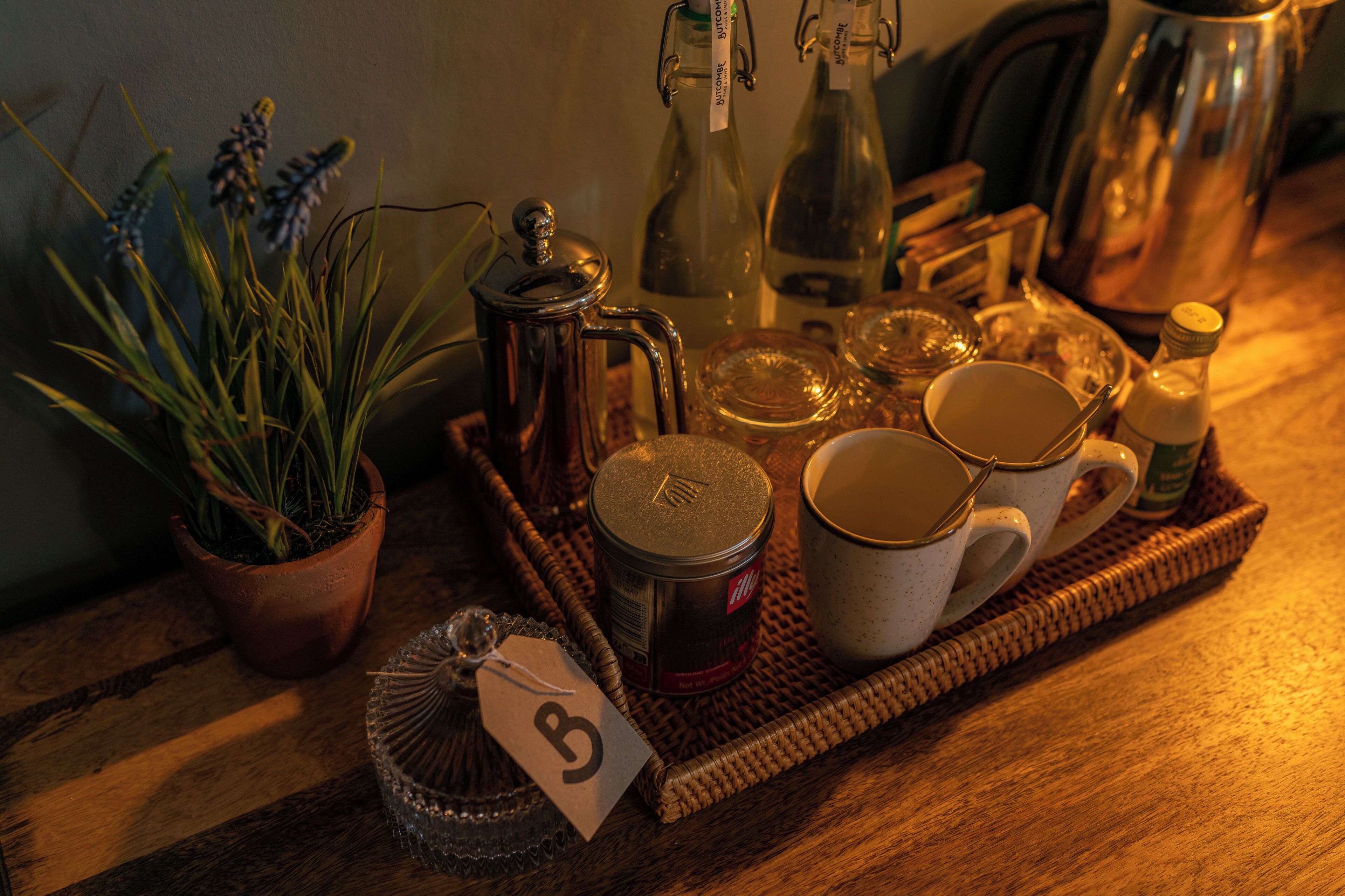 A wooden table with a tray holding a teapot, a glass jar, a can, and a mug.