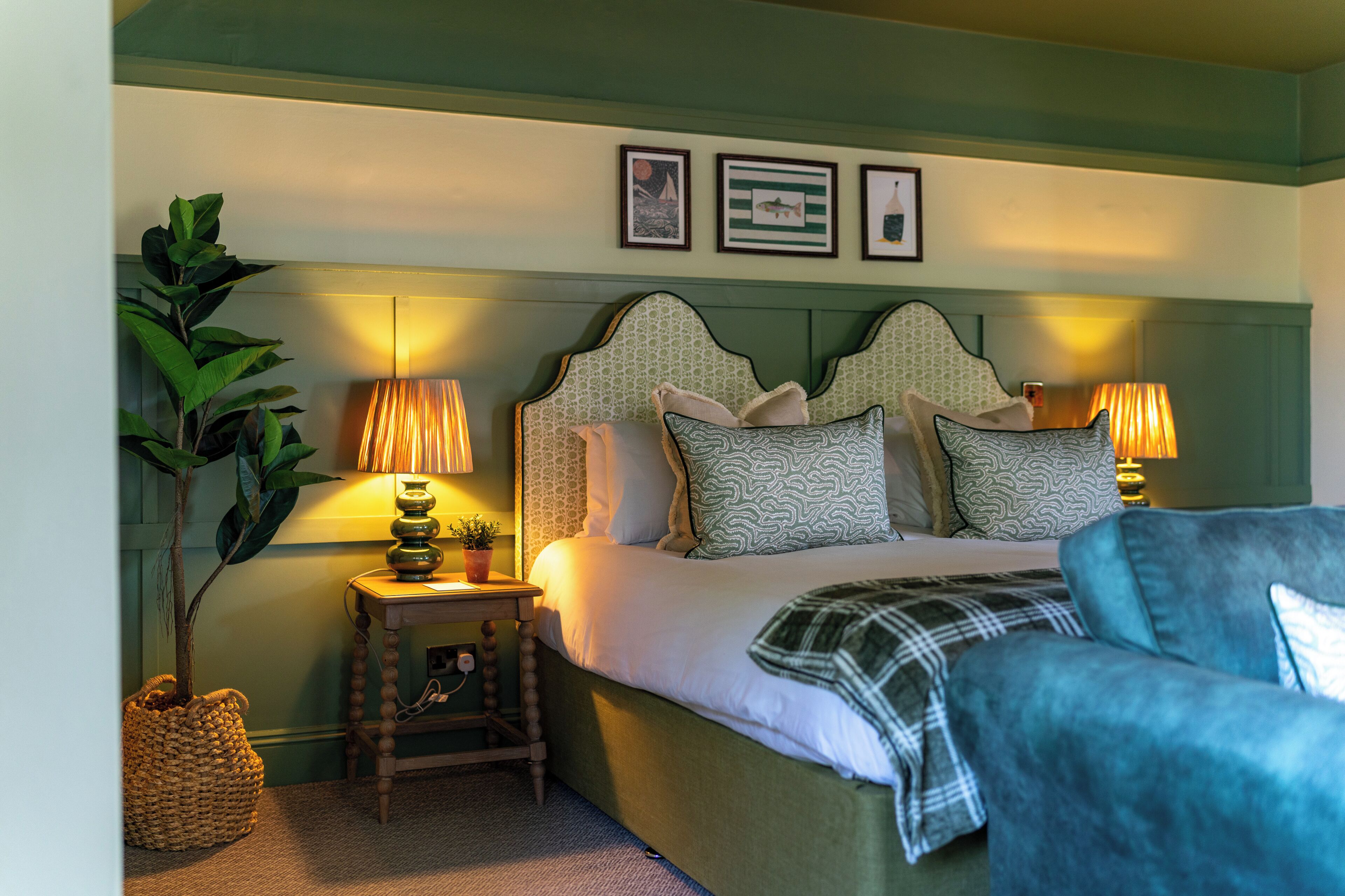 A bedroom with a bed, bedside lamps, a bedside table, a potted plant, and wall art.