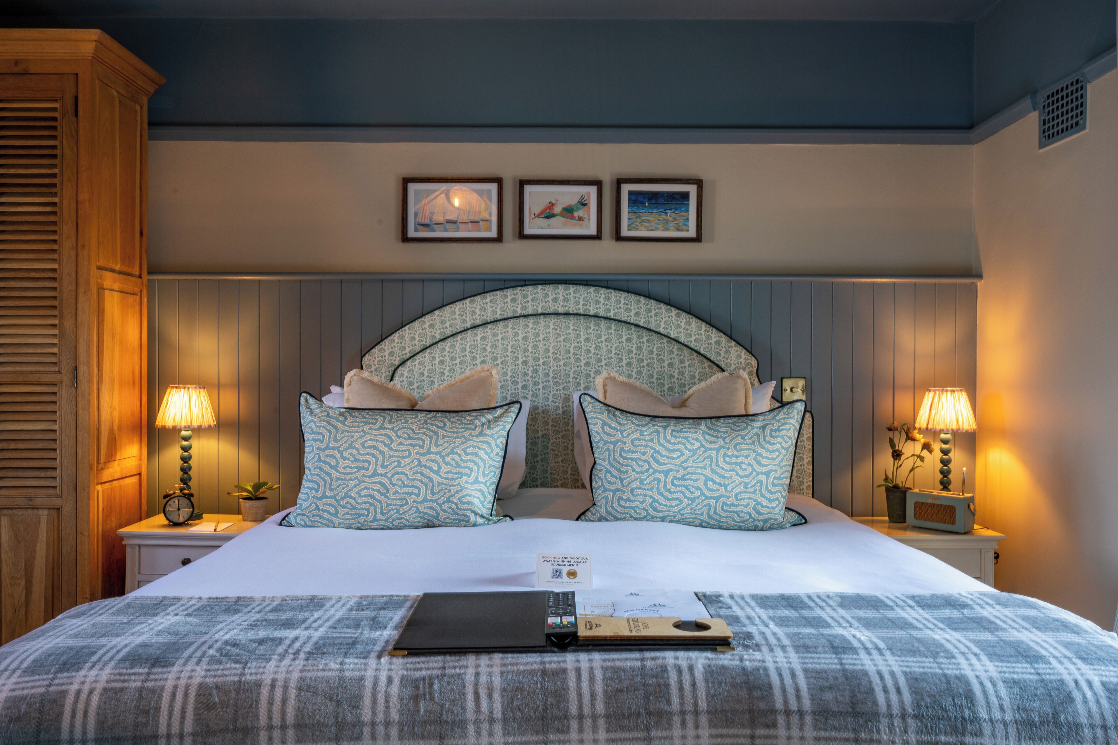 A neatly made bed with patterned pillows, a bedside table with a lamp, and a framed artwork above the bed.