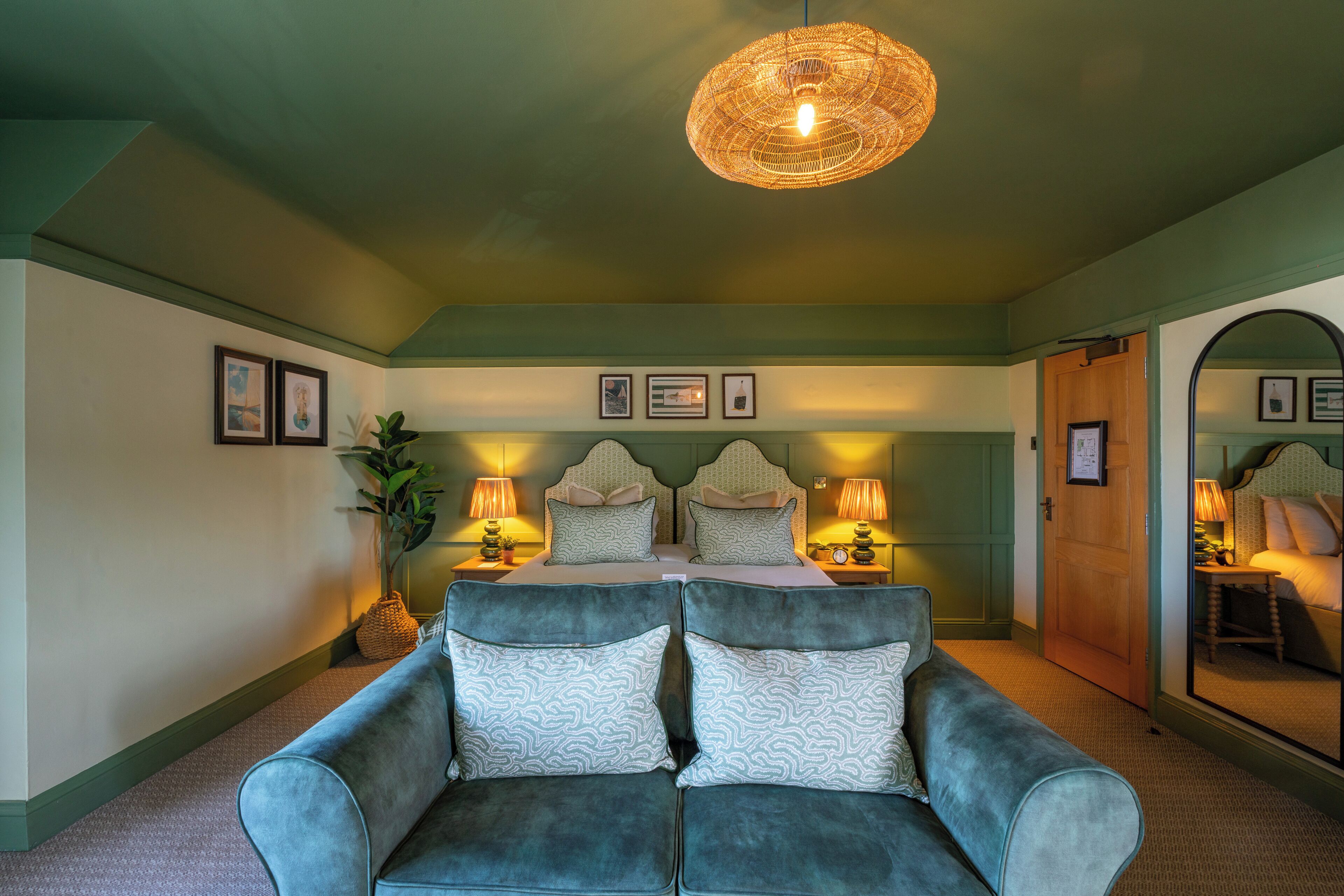 A room with a bed, two bedside lamps, a mirror, and a blue sofa with patterned cushions.