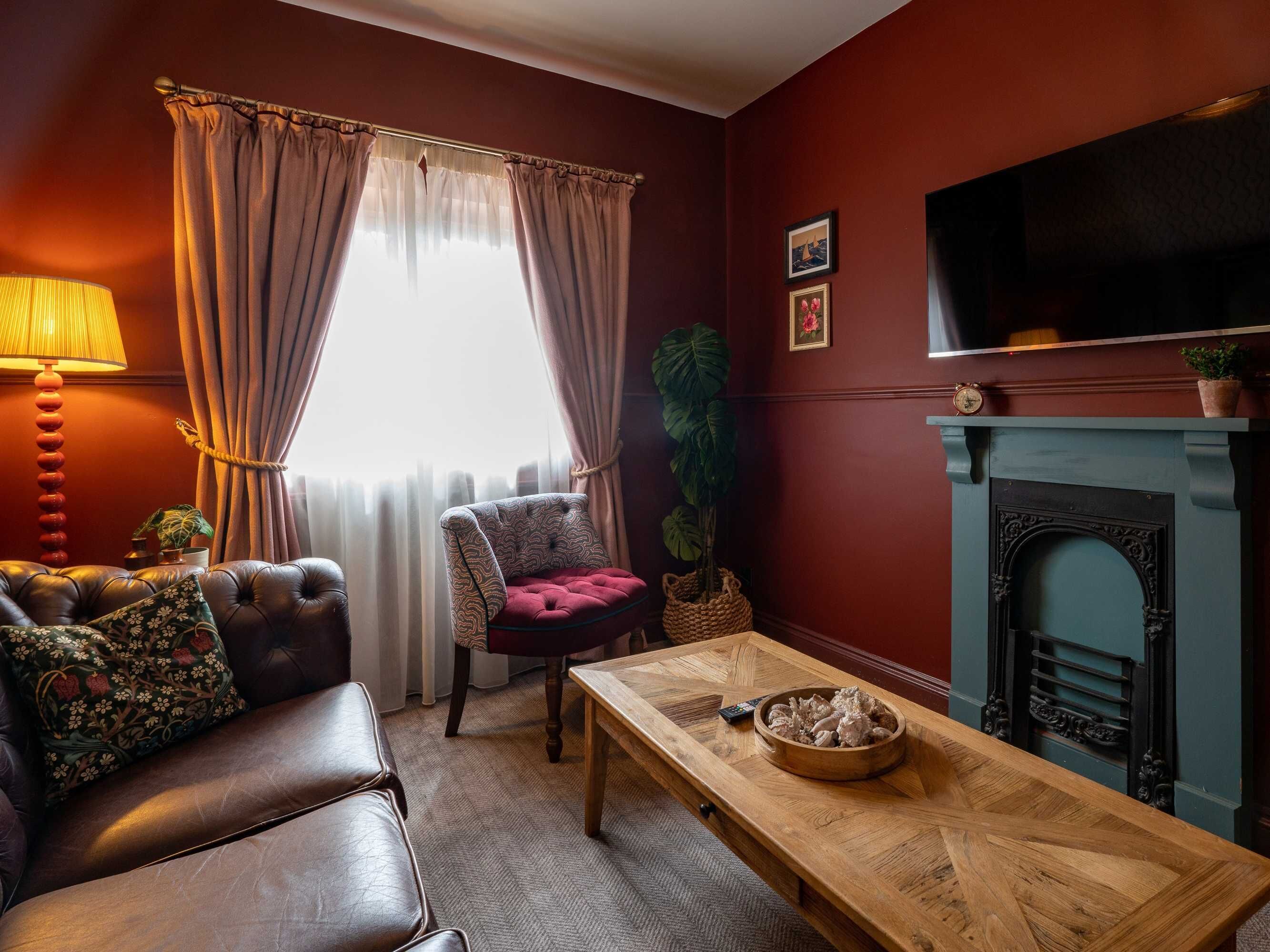 Una sala de estar con un sofá de cuero, un sillón estampado, una mesa de centro de madera, una chimenea y un televisor montado en la pared.