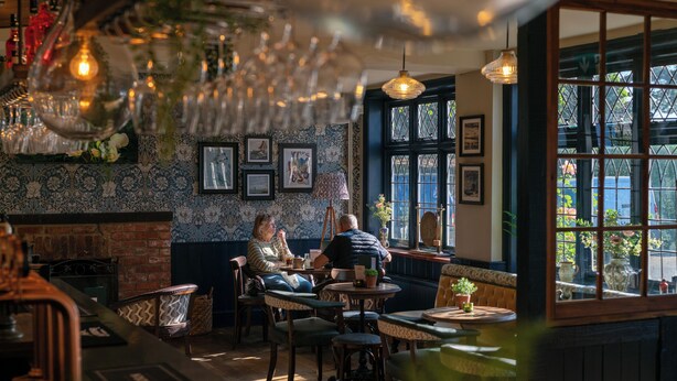 A cozy interior with a fireplace, wooden furniture, and framed pictures on the wall. - The Mayflower (Lymington)