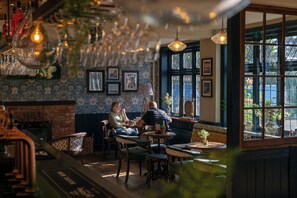 A cozy interior with a fireplace, wooden furniture, and framed pictures on the wall. - The Mayflower (Lymington)