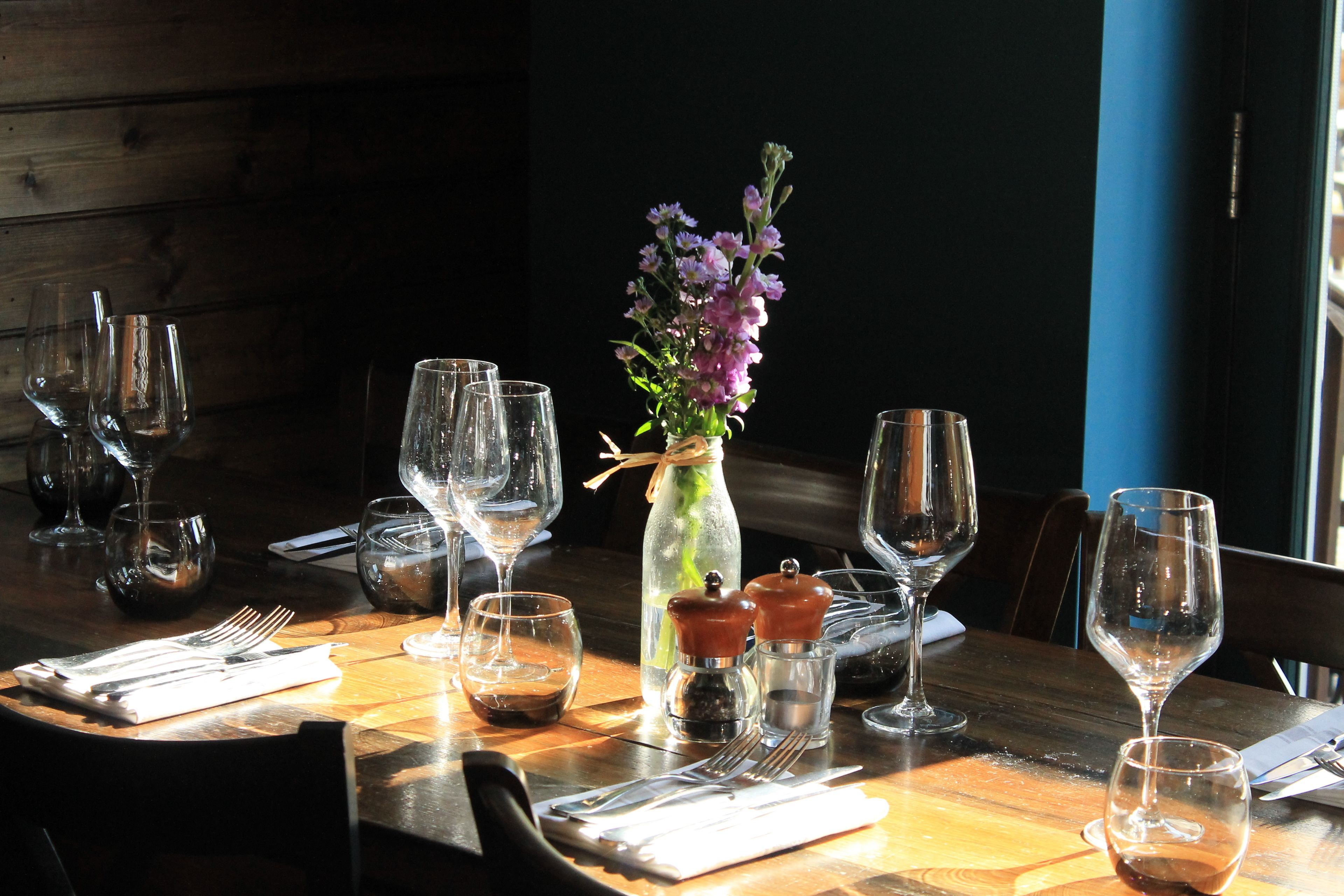 Una mesa de comedor dispuesta con copas de vino, un florero con flores y condimentos.