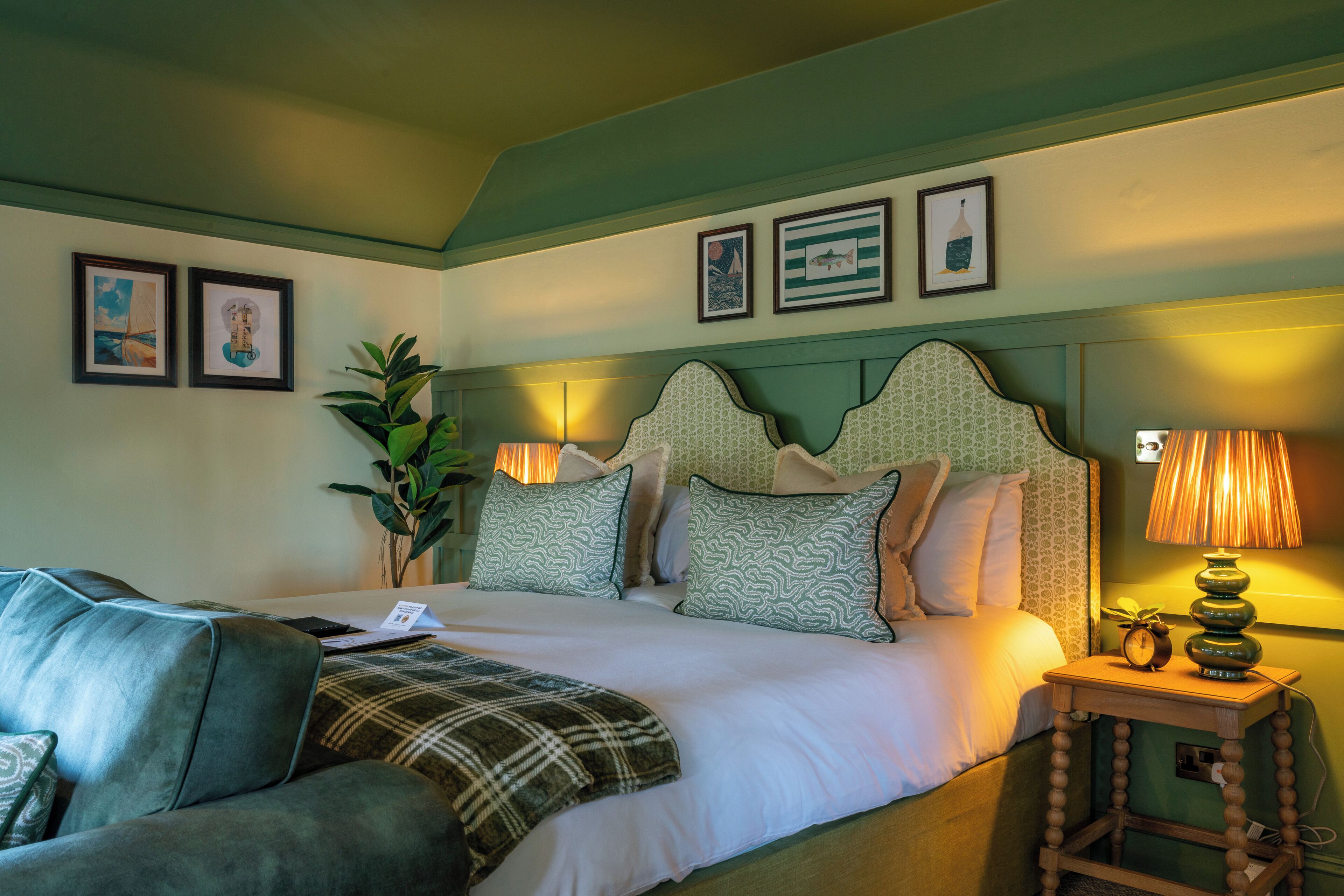 Un dormitorio ordenado con una cama, una mesita de noche con lámpara y un sofá tapizado en verde.