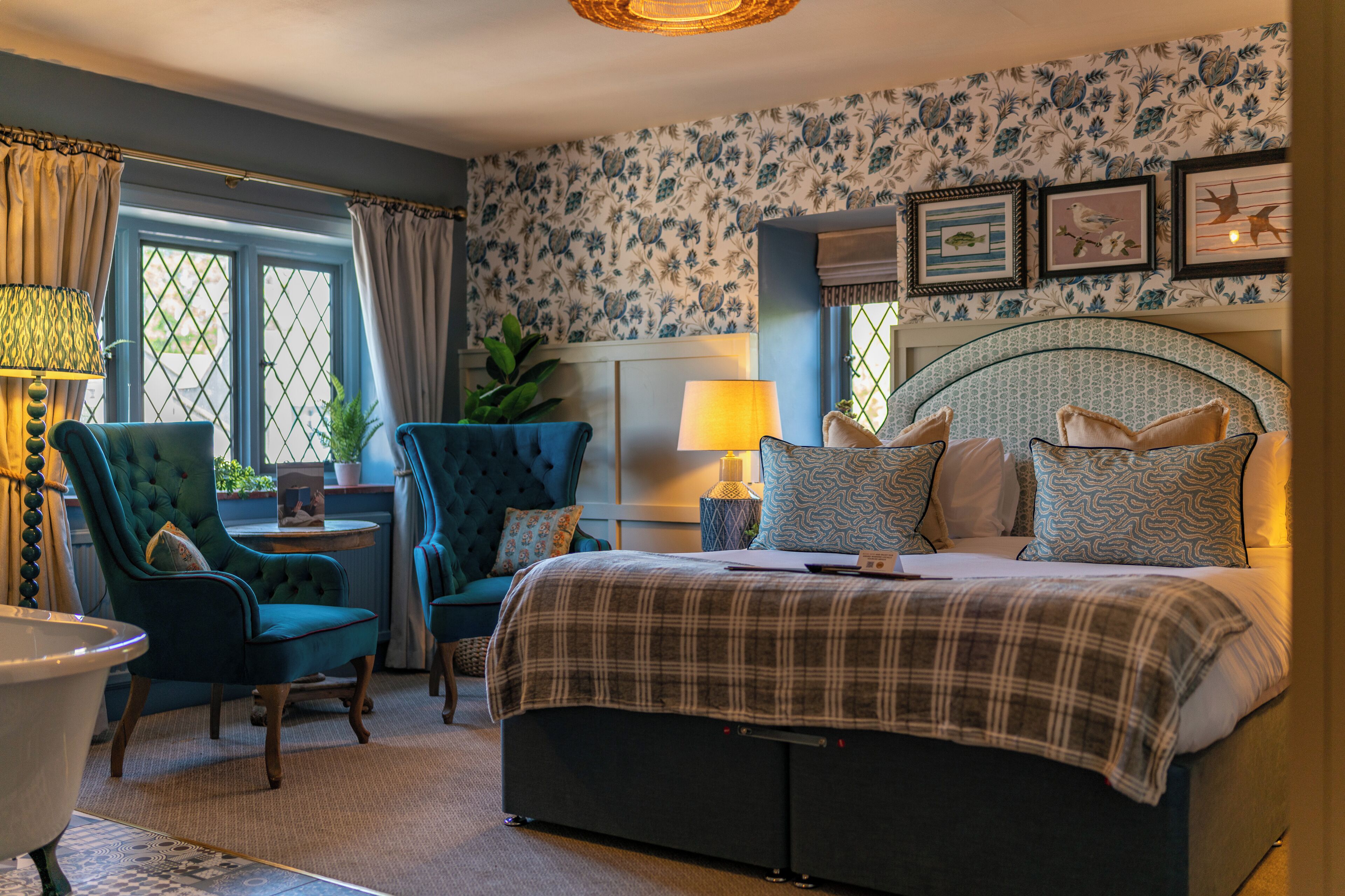 A bedroom with a bed, two armchairs, a table, a lamp, and a window with curtains.