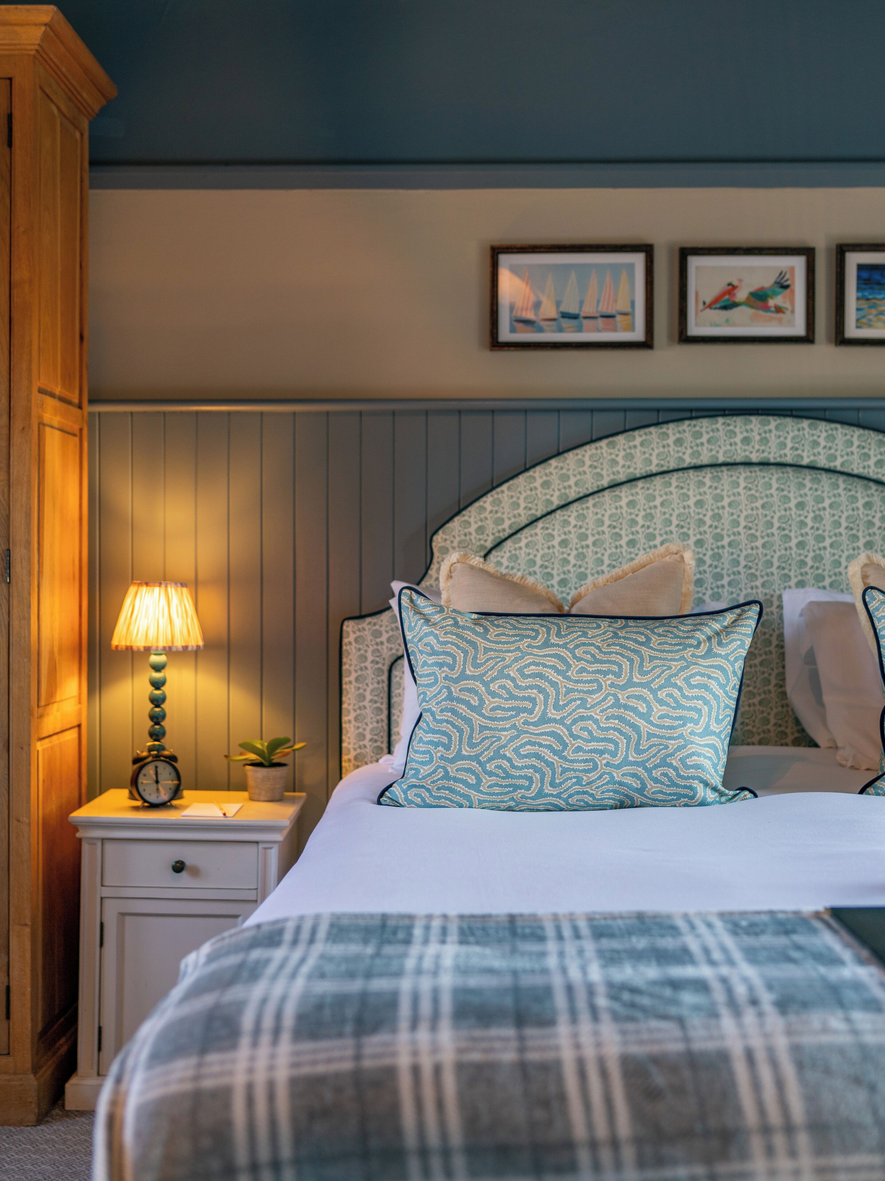 A bedroom with a bed, a nightstand with a lamp, a clock, and framed pictures on the wall.