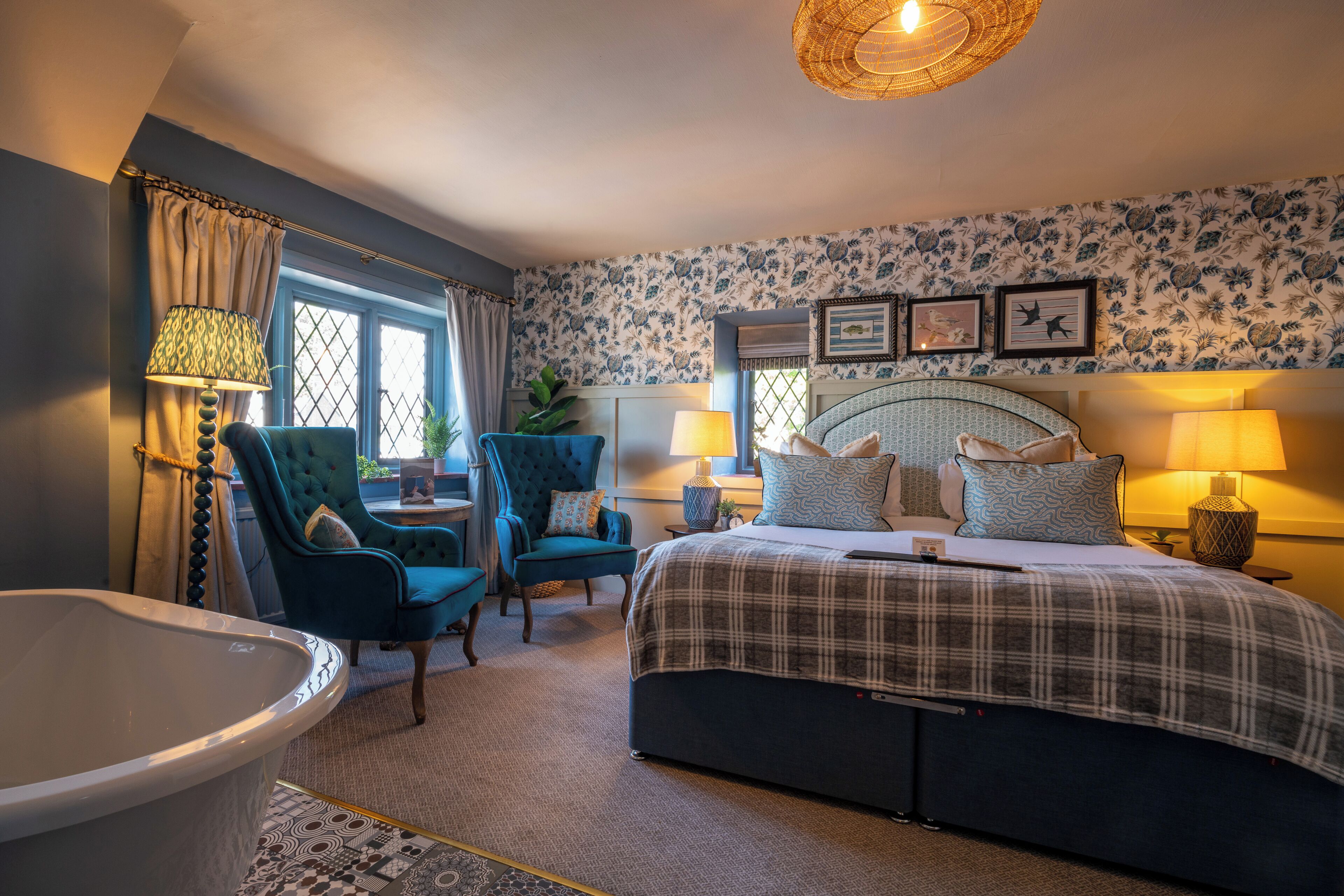 A bedroom with a bed, two chairs, a bathtub, and a window with curtains.