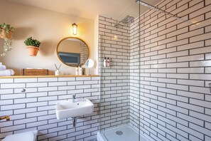 A bathroom with a white sink, mirror, and shower. - The Mayflower (Lymington)