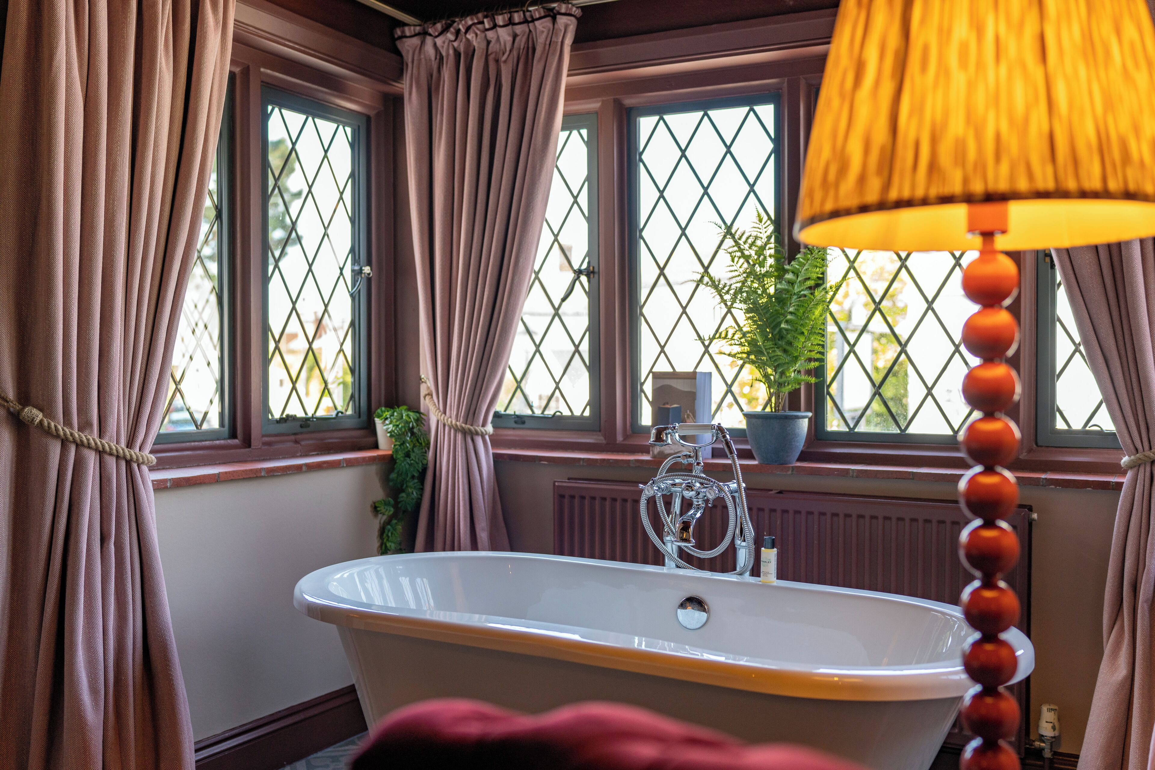 Une salle de bain avec une baignoire sur pieds, une fenêtre avec vue et une lampe.