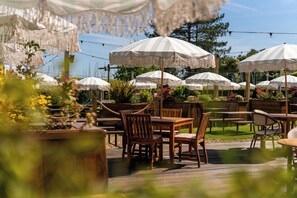 An outdoor seating area with wooden tables and chairs, surrounded by white striped umbrellas. - The Mayflower (Lymington)