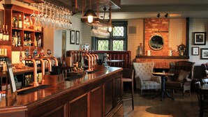 A bar area with multiple taps, glasses, and a brick wall. There are chairs and a table in the seating area. - The Mayflower (Lymington)