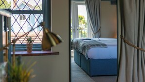 A bedroom with a bed, a window with curtains, a lamp, and a view of the outside. - The Mayflower (Lymington)