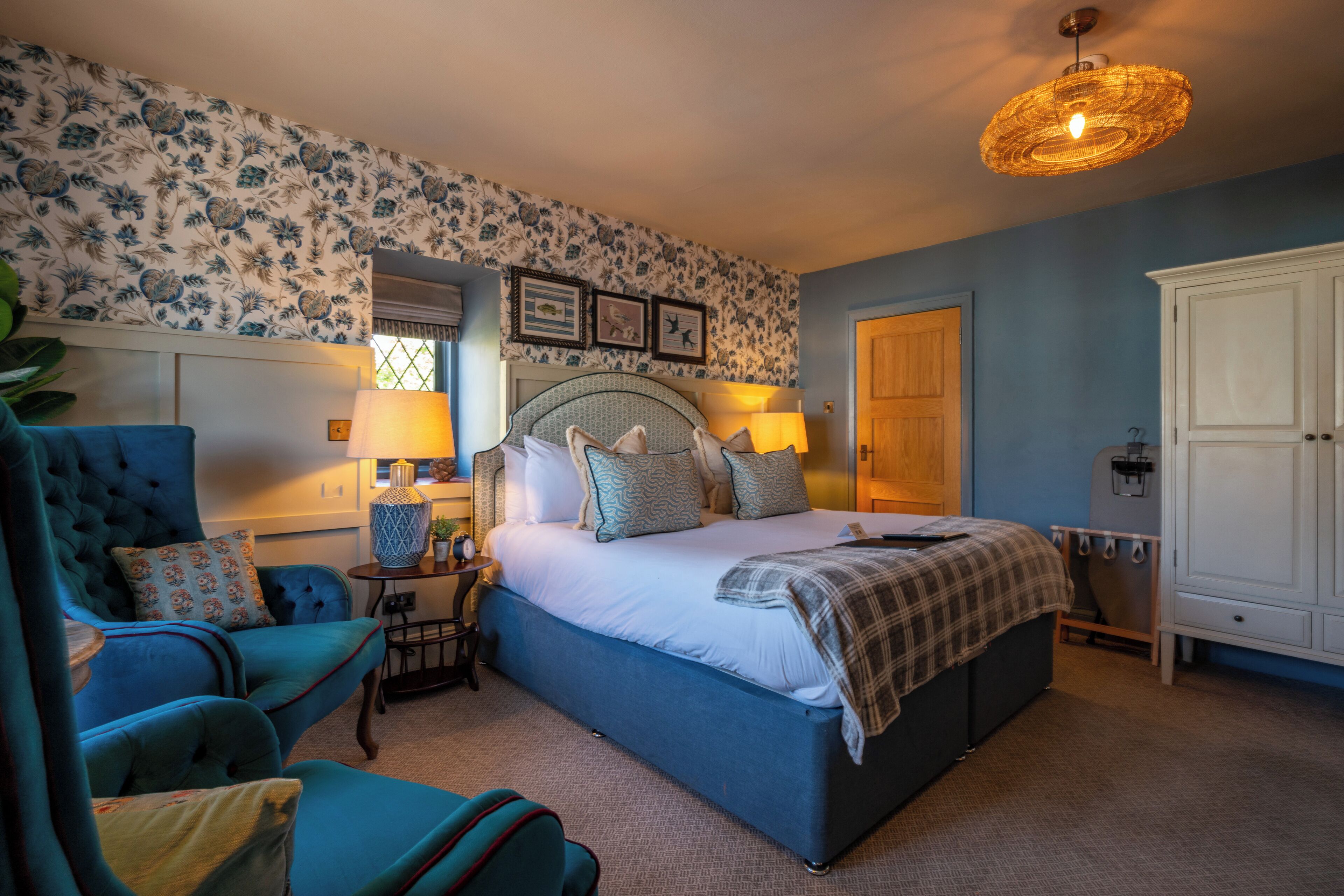 A bedroom with a large bed, a blue armchair, a bedside table with a lamp, and a wardrobe.
