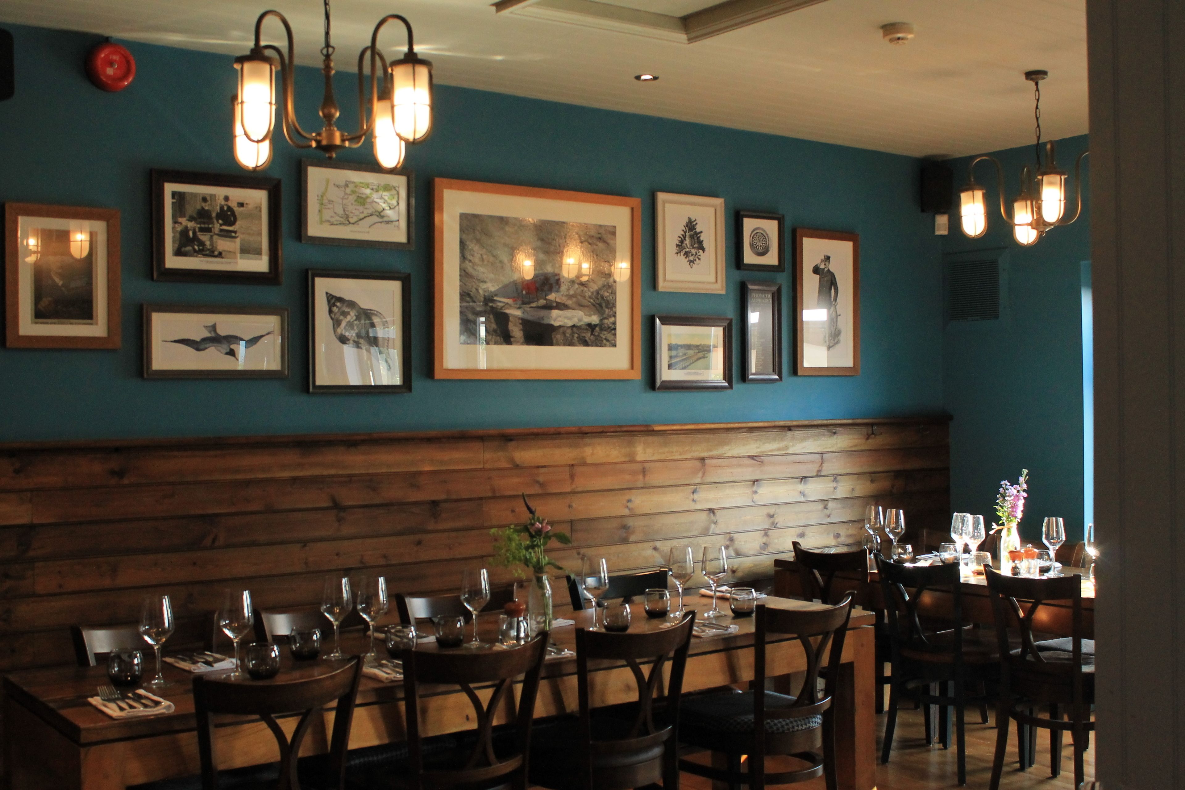 A restaurant with wooden benches and tables, framed artwork on the wall, and hanging light fixtures.