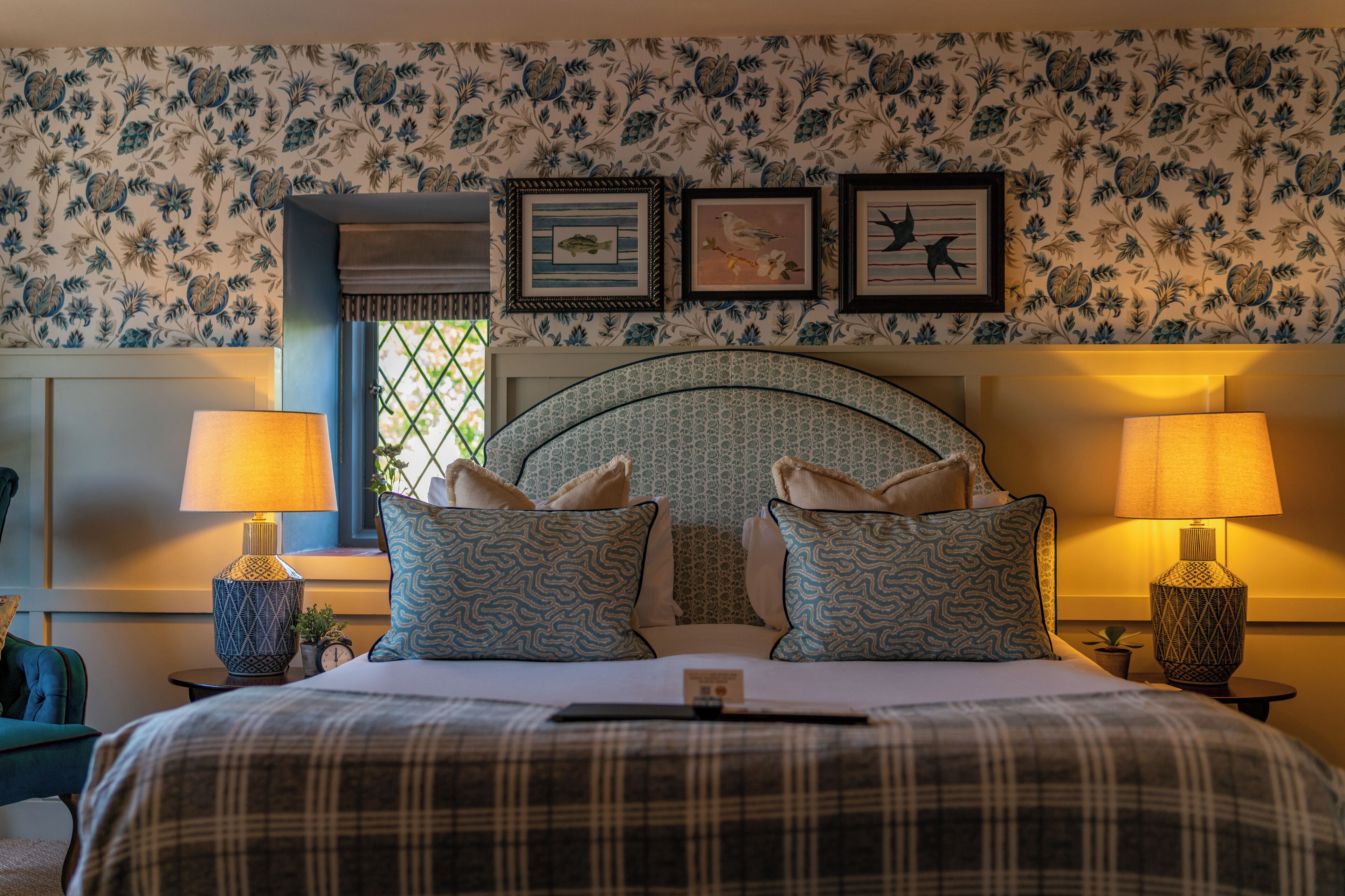 A hotel room with a bed, two nightstands, a window, and floral wallpaper.