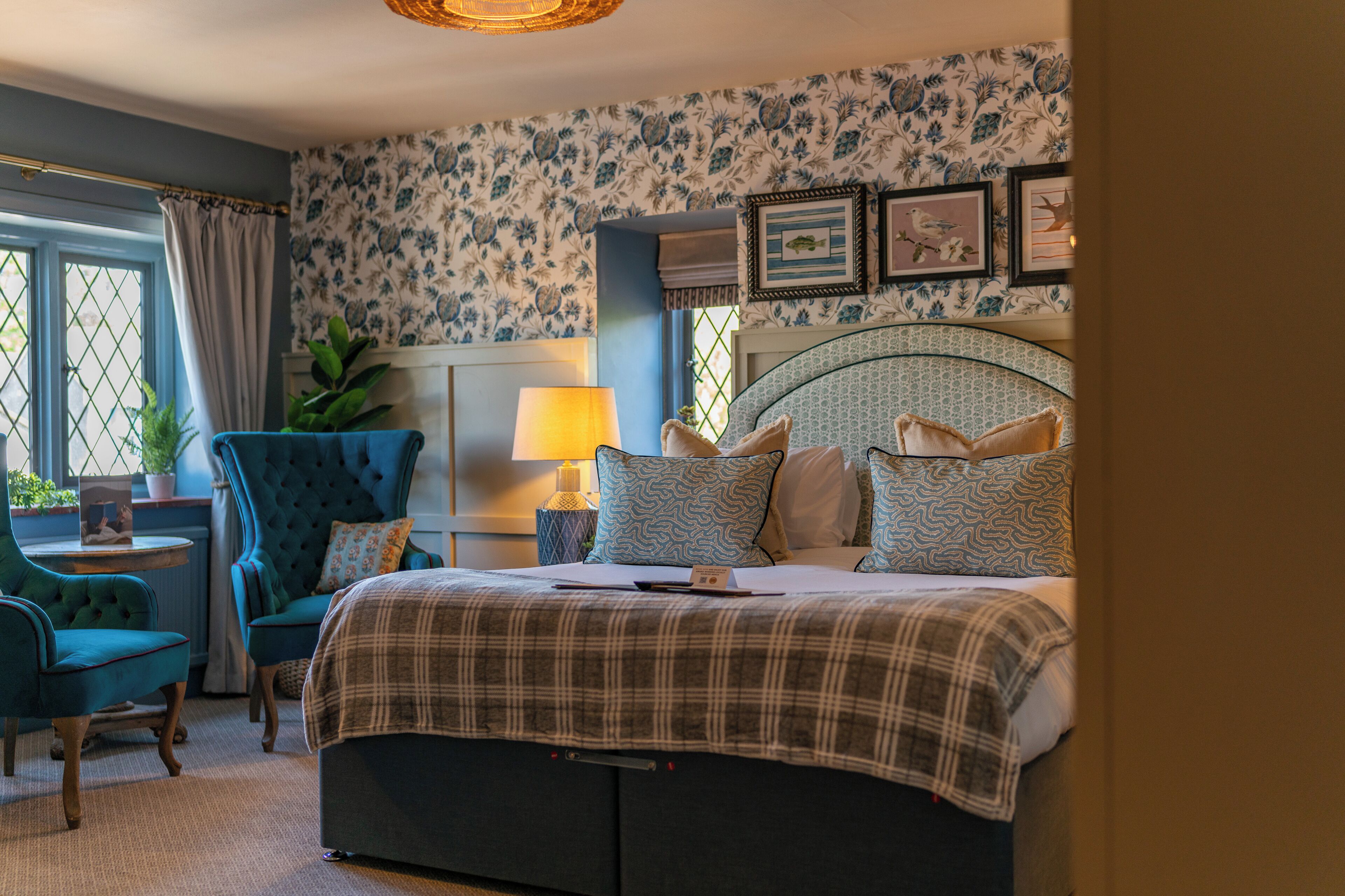 Een slaapkamer met een bed, een stoel, een lamp en een muur met ingelijste foto's.