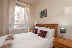 Uma cama bem arrumada com almofadas brancas e vinho, uma cabeceira de madeira e uma mesa de cabeceira com um abajur.