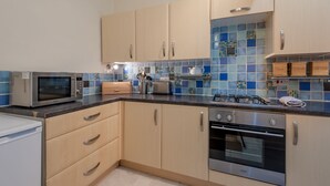 A modern kitchen with light wood cabinets, a stainless steel microwave, a gas stove, and a built-in oven. - Edinburgh Rossie Apartment (Edinburgh)