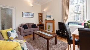 A living room with a sofa, a coffee table, a fireplace, a television, and a window with curtains. - Edinburgh Rossie Apartment (Edinburgh)