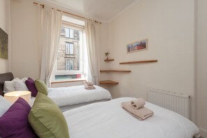 A hotel room with two beds, a window with curtains, a radiator, and a painting on the wall. - Edinburgh Rossie Apartment (Edinburgh)